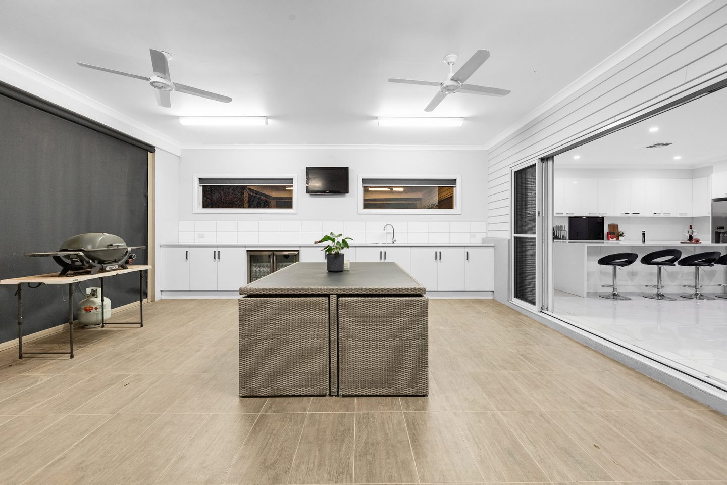 Enclosed alfresco with cabinetry, sink, ceiling fans and sliding doors to the kitchen